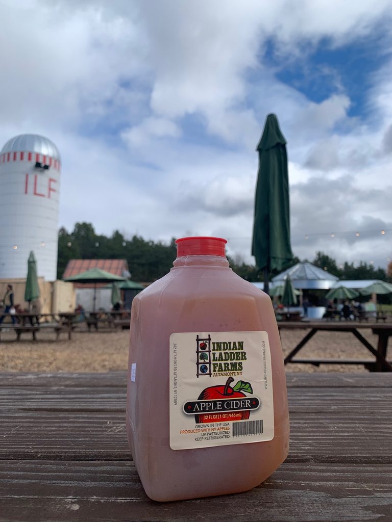 A small jug of apple cider sits on a wooden picnic table.