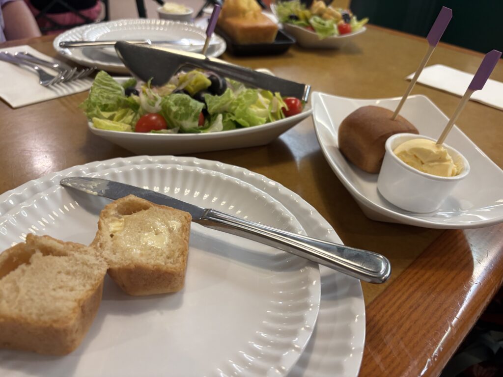 A table with a dinner roll and butter and side garden salad.