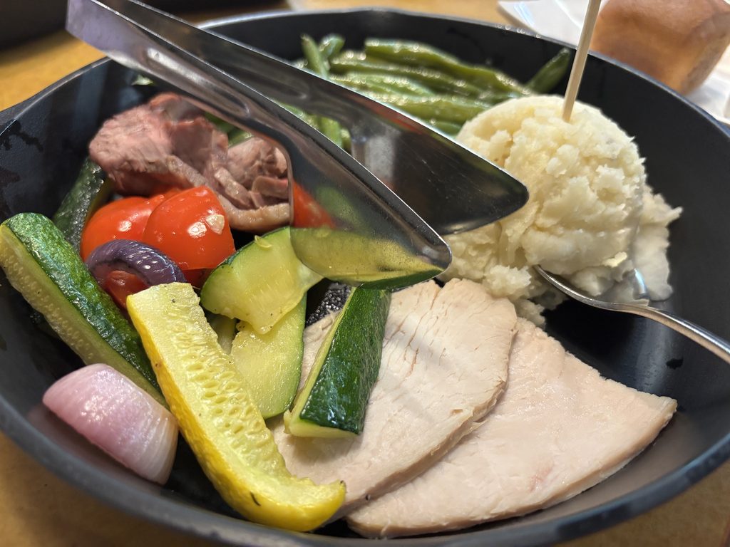 A skillet with fresh vegetables, turkey, beef, and mashed potatoes. 