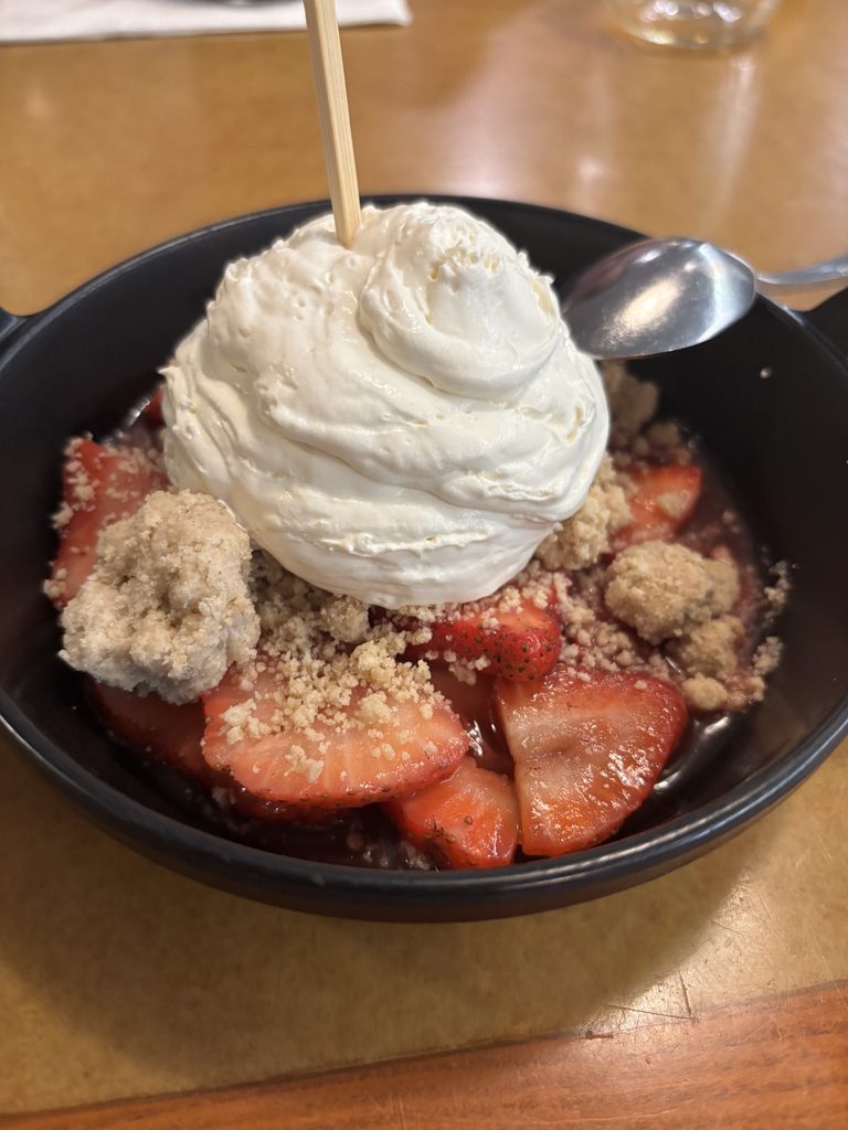 A skillet containing strawberries, a crumble topping, and whipped cream.